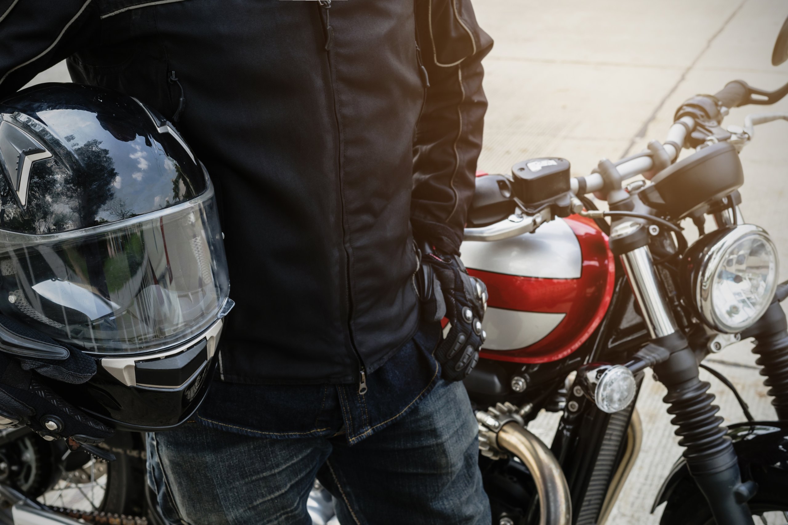 A rider in a leather jacket holding a helmet beside a motorcycle